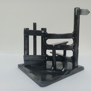 Könnte beinhalten: Eine schwarze Metallsculptur eines Zauns mit einer Bank und einem Wegweiser. Die Skulptur ist aus geschweißtem Metall gefertigt und hat einen rustikalen, industriellen Look.