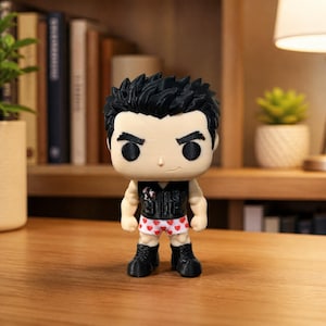 Puede incluir: Una figura de vinilo estilizada con cabello negro puntiagudo, tez clara y una pequeña sonrisa. La figura viste un chaleco negro sin mangas sobre ropa interior blanca con estampado de corazones rojos pequeños, botas negras y una complexión musculosa.