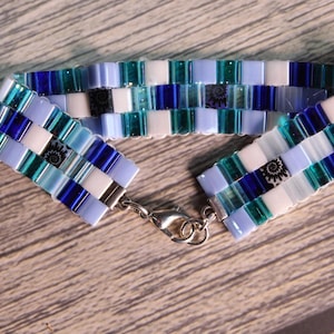 May include: A blue, white and green beaded bracelet with a silver clasp. The beads are arranged in a chequered pattern.