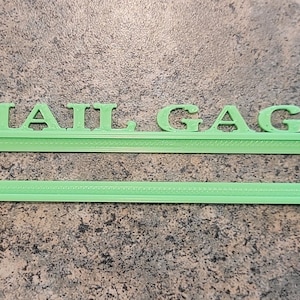 May include: A green plastic mail holder with the words "MAIL GAGE" printed on the top.
