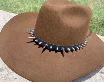 May include: A brown felt cowboy hat with a black leather band and silver spikes around the crown.