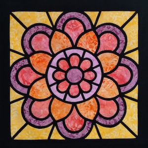 May include: A colorful stained glass style quilt block with a purple, pink, and orange flower design. The flower has a central circle with a smaller purple circle in the center.