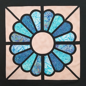 May include: A pink and blue stained glass design with a circular center and a flower-like pattern. The design is framed in black.