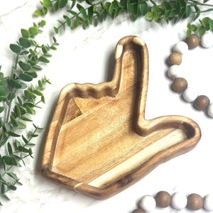 May include: A wooden hand-shaped dish with a natural wood finish. The dish is shaped like a hand giving a thumbs up gesture.