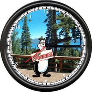May include: A black and white clock with a cartoon bear holding a sign that says "Hamm's". The clock face has a picture of a lake and trees.