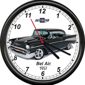 May include: A black and white wall clock featuring a 1957 Chevrolet Bel Air. The clock face has black hands and a white background with black numbers. The clock is framed in a black circle with a silver rim.