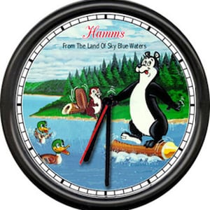 May include: A black and white clock with a picture of a bear water skiing on a log. The clock face has the words "Hamms From The Land Of Sky Blue Waters".