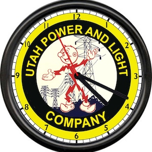 May include: A round wall clock with a black frame and a yellow border featuring the text UTAH POWER AND LIGHT COMPANY. The center displays a cartoon character made of red lightning bolts standing in front of black electrical transmission towers.