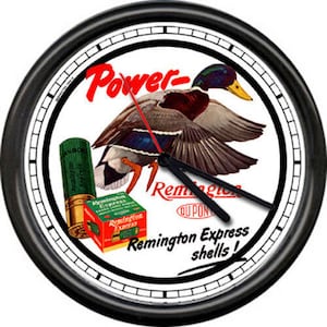 May include: A black and white clock with a vintage advertisement for Remington Express shells. The ad features a mallard duck in flight with the text "Power - Remington  OU PONT  Remington Express shells!"