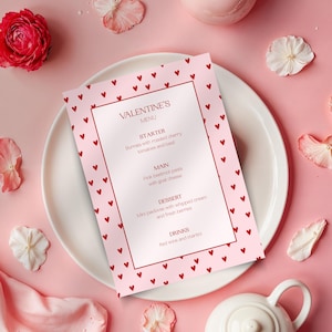 May include: A Valentine's Day menu on a white plate, featuring a pink background with red hearts. The menu lists a starter, main course, dessert, and drinks. The menu is surrounded by decorative flowers and a teapot.