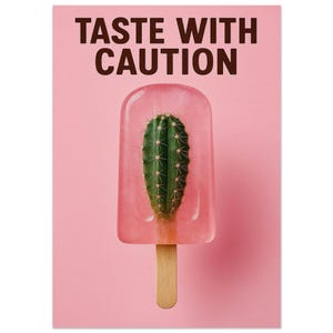May include: A pink background with a popsicle containing a green cactus. The popsicle has a wooden stick. The text "TASTE WITH CAUTION" is at the top of the image.