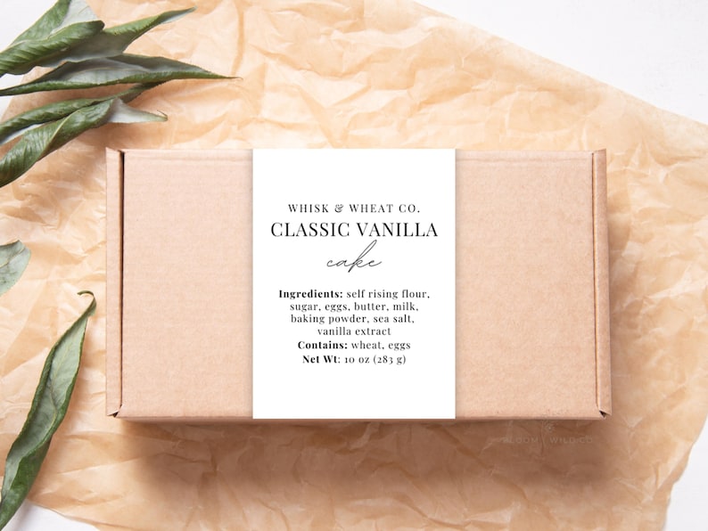 May include: A brown box with a white label that reads "WHISK & WHEAT CO. CLASSIC VANILLA cake" and lists the ingredients: self rising flour, sugar, eggs, butter, milk, baking powder, sea salt, vanilla extract. It also states "Contains: wheat, eggs" and "Net Wt: 10 oz (28 g)".