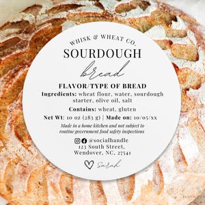 May include: White round label with black text that reads "Whisk & Wheat Co. Sourdough bread Flavor/Type of Bread Ingredients: wheat flour, water, sourdough starter, olive oil, salt Contains: wheat, gluten Net Wt: 10 oz (283 g) | Made on: 10/05/XX Made in a home kitchen and not subject to routine government food safety inspections @socialhandle 123 South Street, Wendover, NC, 27541 Sarah"
