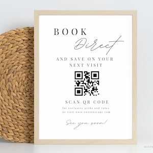 以下が含まれることがあります： 「BOOK Direct」と「AND SAVE ON YOUR NEXT VISIT」と書かれた黒い文字の白い額入りの看板。QRコードと「SCAN QR CODE」と「See you soon!」の文字が含まれています。左側には織りのバスケットがあります。