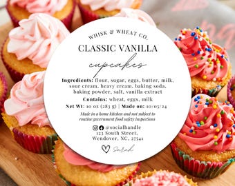 May include: A white circle sticker with black text that reads "WHISK & WHEAT CO. CLASSIC VANILLA cupcakes". The sticker lists the ingredients, contains, net weight, and date made. The sticker is placed on a wooden surface with pink and white cupcakes with colorful sprinkles.