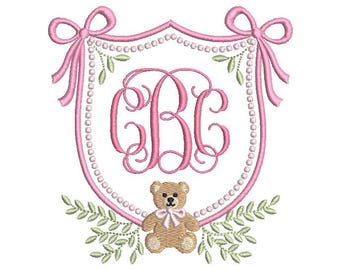 May include: An embroidery design featuring a pink shield-shaped frame with pearl-like accents and bows at the top corners. Inside the frame are the pink monogram letters CBC in a script font. A tan teddy bear with a pink bow sits at the bottom.