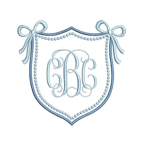 May include: A light blue embroidered shield design with a monogram of the letters "CBC" in the center. The shield is outlined in a darker blue and adorned with a string of pearls and two bows at the top. The design is on a white background.