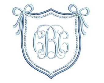 May include: A light blue embroidered shield design with a monogram of the letters "CBC" in the center. The shield is outlined in a darker blue and adorned with a string of pearls and two bows at the top. The design is on a white background.