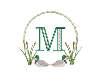 Könnte beinhalten: Ein grünes Monogramm des Buchstabens M mit einem Kranz aus grünen Schilf und zwei Stockenten auf jeder Seite.
