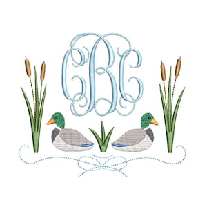 以下が含まれることがあります： 2 羽のアヒル、ガマ、水色のモノグラムをあしらった刺繍デザイン。アヒルは緑色の頭とオレンジ色のくちばしをしています。デザインは白い背景にあります。