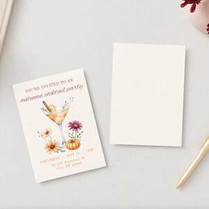 May include: An invitation card for an autumn cocktail party. The card features a watercolor illustration of a cocktail, flowers, and a pumpkin. The text reads "You're invited to an autumn cocktail party". A blank card and a gold pen are also present.