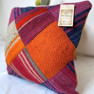 May include: A colorful patchwork pillow with a tag that reads "VP munay" and includes social media icons. The pillow is made of woven fabric in shades of pink, orange, blue, and gray.