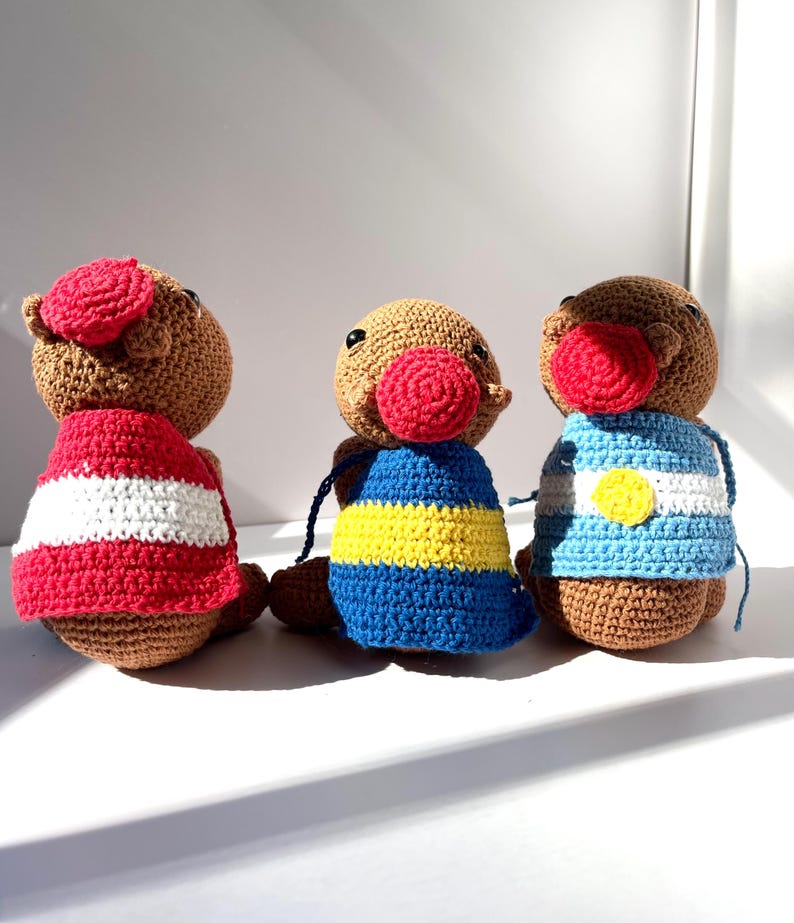 Op de afbeelding: Drie handgemaakte gehaakte poppen met bruine lichamen, rode neuzen en verschillende outfits. E&eacute;n pop draagt een rood-wit gestreept shirt, een andere een blauw-geel gestreept shirt en de derde een blauw-wit gestreept shirt.