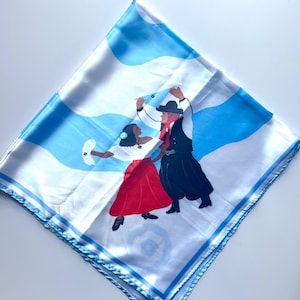 May include: Square white scarf with a blue and white wavy pattern and a border. The scarf features an illustration of two people dancing in traditional clothing. The woman wears a red skirt and the man wears a black outfit.