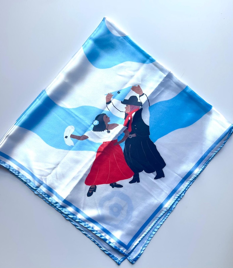 May include: Square white scarf with a blue and white wavy pattern and a border. The scarf features an illustration of two people dancing in traditional clothing. The woman wears a red skirt and the man wears a black outfit.