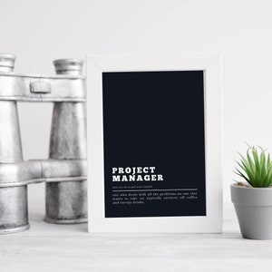May include: A white framed print with the words "PROJECT MANAGER" in bold white text. Below the title is a definition: "one who deals with all the problems no one else wants to take on, typically survives off coffee and energy drinks."