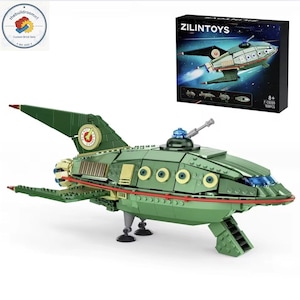 May include: A green and tan brick-built spaceship model with a box labeled "ZILINTOYS." The spaceship has a retro design with a cockpit, wings, and a tail fin. The box shows a similar spaceship design. The model is suitable for ages 8+.