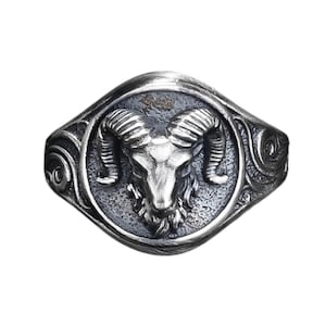 Może przedstawiać: Srebrny pierścień z detalicznym wzorem głowy barana. Pierścień ma fakturowany, ozdobny pasek.