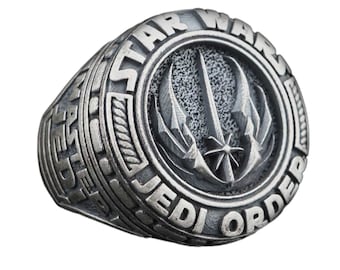 May include: A silver ring with a raised circular design featuring the Star Wars Jedi Order logo. The ring is inscribed with "Star Wars Jedi Order".