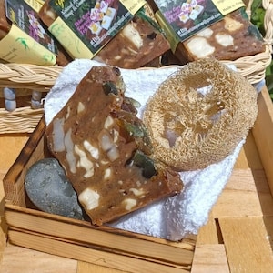 May include: A close-up of a brown and white bar of soap with a loofah sponge and a small wooden box. The soap is labeled "Yedid Natural Artisan Soap & Cosmetics Co. Skin Care Facial Soap".
