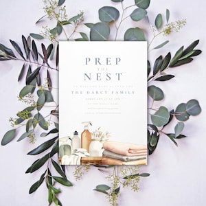 May include: A white invitation card with the text "Prep the Nest" in blue and pink lettering. The invitation is for a baby shower to welcome a new baby into the Darcy family. The date and time of the event are listed as February 17 at 1 pm. The invitation also includes a watercolor illustration of a basket with baby supplies, including bottles, towels, and a spray bottle.