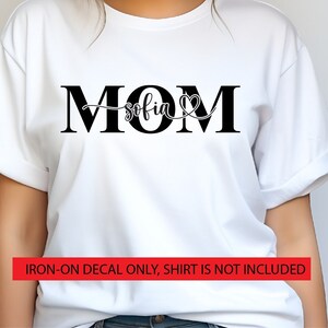 May include: White t-shirt with black text that reads "MOM sofia" with a heart symbol. Iron-on decal only, shirt is not included.