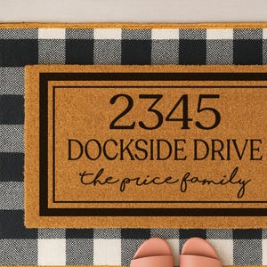 May include: A brown coir doormat with black trim and white lettering. The doormat has the address "2345 Dockside Drive" and the text "the price family".