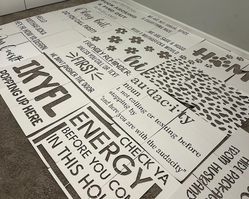 May include: A collection of white stencils with black text and various designs. The stencils feature phrases like "Energy Before You Come In This House" and "Audacity". Some stencils have floral and paw print designs.