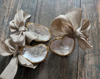 Portatarjetas personalizados con forma de ostra, con lazo, caligrafía en perla y ribete dorado.