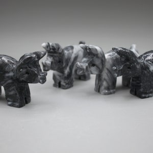 May include: A collection of five marble pig figurines. Each pig is carved with a detailed design, showcasing a mix of black and white marbling. The pigs are arranged in a row, with their heads facing forward.