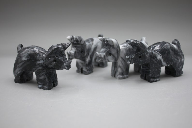 May include: A collection of five marble pig figurines. Each pig is carved with a detailed design, showcasing a mix of black and white marbling. The pigs are arranged in a row, with their heads facing forward.