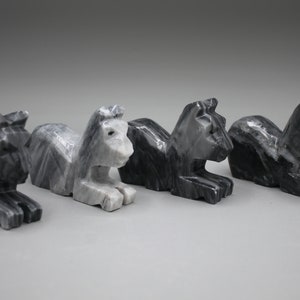 May include: Four carved stone lion sculptures in varying shades of gray and black. Each lion is in a seated position with its front paws extended. The sculptures have a geometric, angular design.