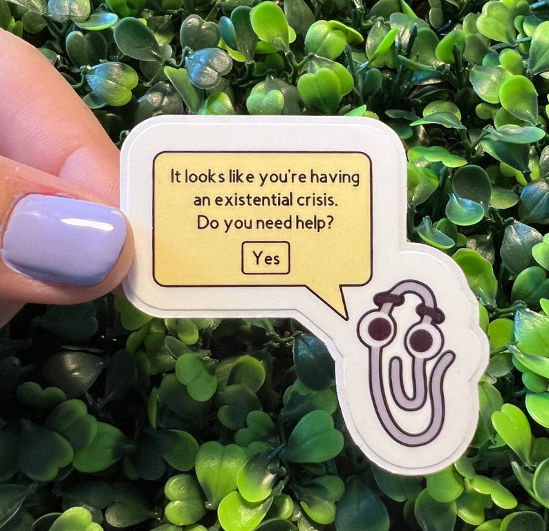 Op de afbeelding: Een gele spraakballon met de tekst "Het lijkt erop dat je een existenti&euml;le crisis hebt. Heb je hulp nodig? Ja" en een cartoon paperclip met ogen en een hoofdband.