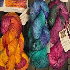 May include: Close-up of colorful yarn skeins in shades of orange, pink, blue, and green. The yarn is arranged in a display, with tags attached. The yarn appears to be a blend of alpaca and other fibers, suitable for knitting or crochet projects.