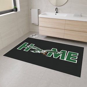 May include: A black and green bath mat with the word "HOME" in green letters and a green eagle flying over the word.