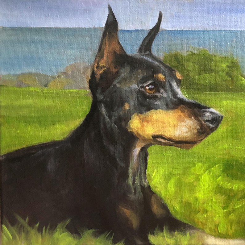 May include: Oil painting of a Doberman Pinscher dog lying in a grassy field. The dog has black fur with tan markings on its snout and chest. The background features a blue sky and a body of water.