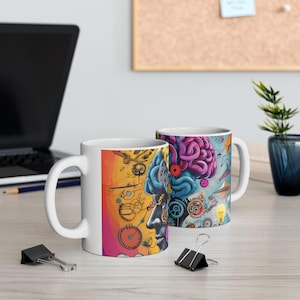May include: Two white ceramic mugs with a colorful brain design. One mug features a side profile with gears and clocks, while the other displays a detailed brain illustration with gears and lightbulbs. The mugs are on a light-colored wooden surface.