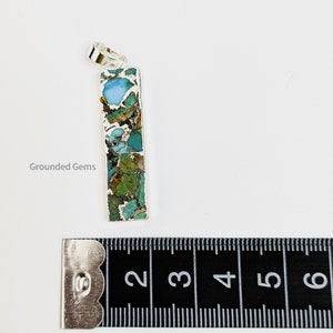 May include: A silver pendant with a rectangular turquoise stone. The stone has a mix of green, blue, and brown colors. The pendant is about 2 inches long.
