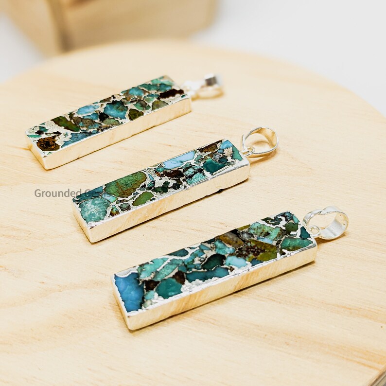 May include: Three silver pendants with turquoise and green stone inlay. The stones are a mix of blue, green, and brown colors. The pendants are rectangular in shape and have a silver bail.