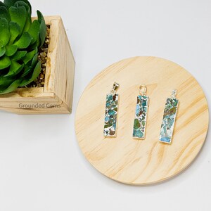 May include: Three silver pendants with a rectangular shape and a green, blue, and brown marbled stone design. The pendants are on a wooden surface.